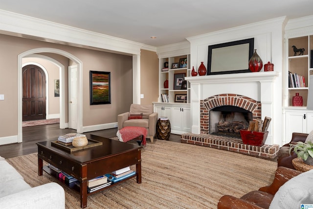 living room featuring a brick fireplace, built in features, ornamental molding, and hardwood / wood-style flooring