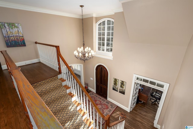 staircase with hardwood / wood-style floors, an inviting chandelier, ornamental molding, and a high ceiling