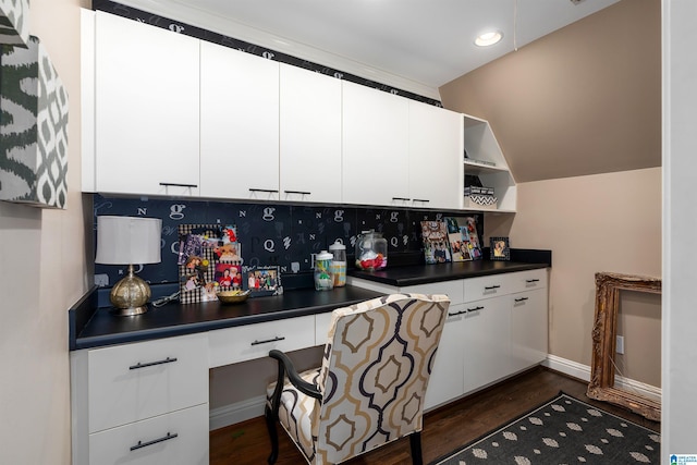 kitchen with dark hardwood / wood-style flooring, backsplash, vaulted ceiling, built in desk, and white cabinets