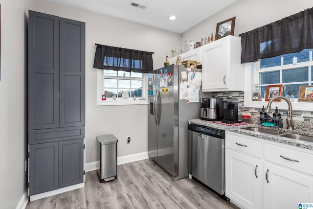 kitchen with white cabinets, sink, light wood-type flooring, light stone counters, and stainless steel appliances