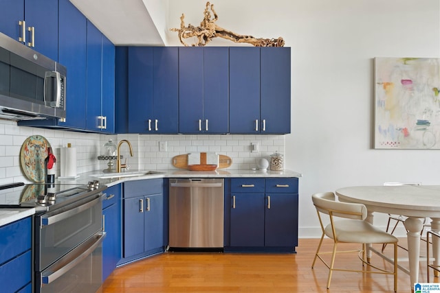 kitchen with blue cabinetry, sink, stainless steel appliances, tasteful backsplash, and light wood-type flooring