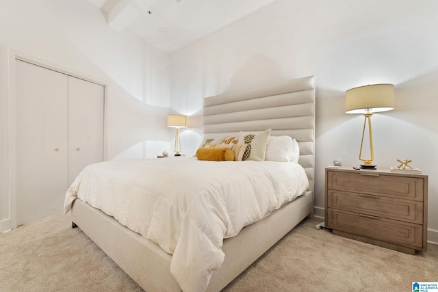 bedroom with beam ceiling, light carpet, and a closet