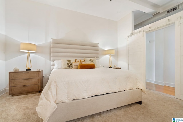 bedroom with beamed ceiling, a barn door, and light colored carpet