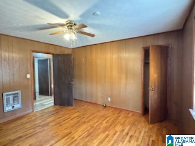 unfurnished room featuring heating unit, ceiling fan, wooden walls, and light hardwood / wood-style flooring