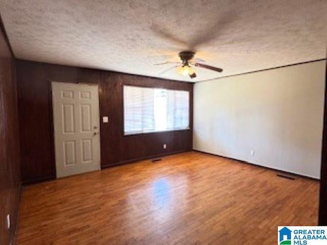 unfurnished room with ceiling fan, hardwood / wood-style floors, wood walls, and a textured ceiling