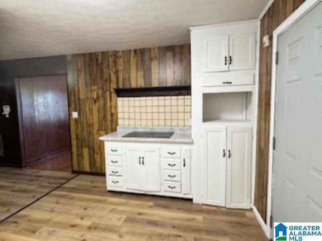 kitchen with black electric stovetop, light wood-type flooring, tasteful backsplash, wooden walls, and white cabinets