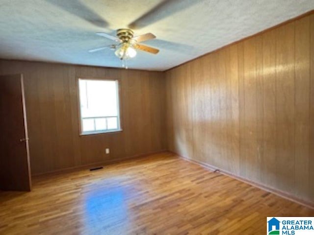 empty room featuring ceiling fan, wooden walls, and light hardwood / wood-style flooring