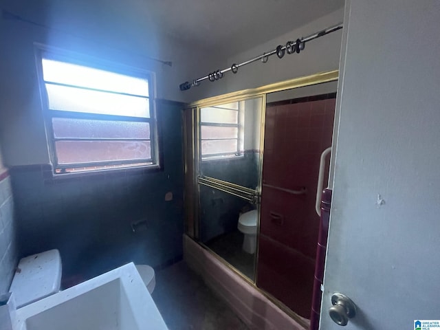 bathroom featuring combined bath / shower with glass door, toilet, and tile walls