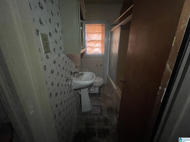 bathroom with toilet, a shower with door, and sink