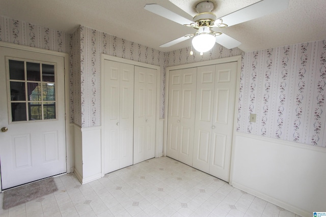 unfurnished bedroom with ceiling fan, a textured ceiling, and two closets