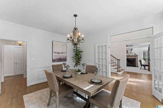 dining space featuring french doors, light hardwood / wood-style flooring, ornamental molding, and a notable chandelier