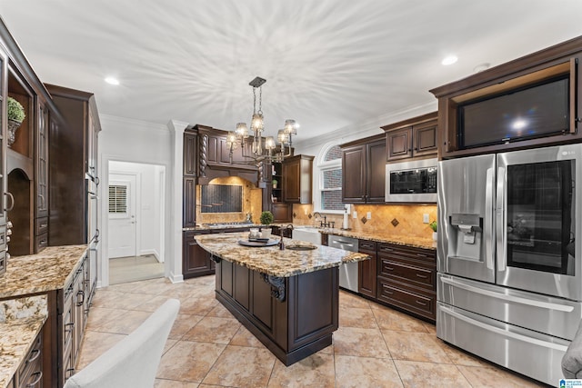 kitchen with appliances with stainless steel finishes, light stone counters, ornamental molding, decorative light fixtures, and a center island