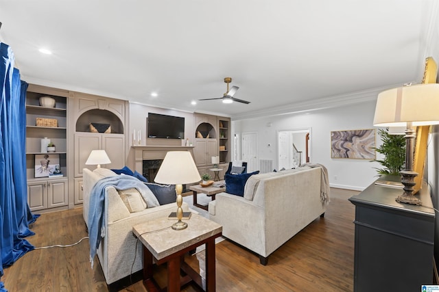 living room with ceiling fan, crown molding, dark wood-type flooring, and built in shelves