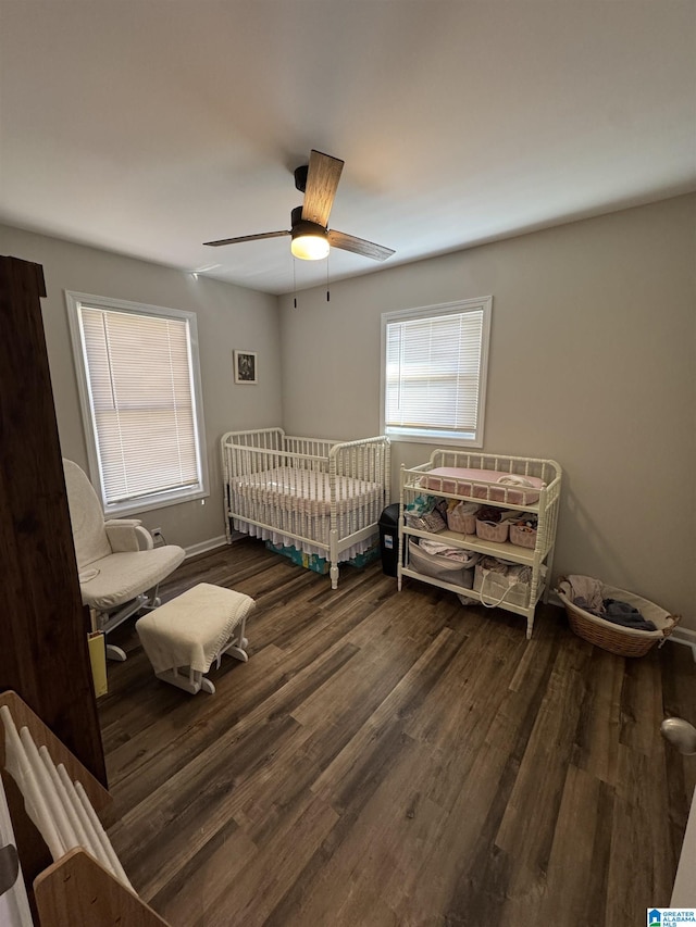 bedroom with ceiling fan, dark hardwood / wood-style flooring, and a nursery area