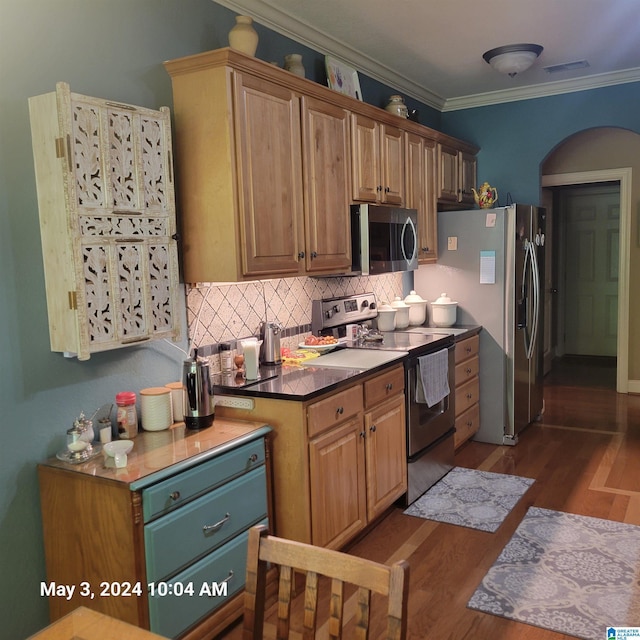 kitchen featuring tasteful backsplash, arched walkways, ornamental molding, wood finished floors, and stainless steel appliances