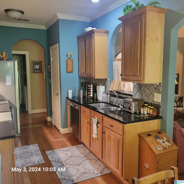 kitchen with a sink, dark countertops, crown molding, and stainless steel dishwasher