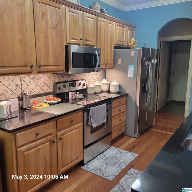 kitchen with tasteful backsplash, dark countertops, appliances with stainless steel finishes, wood finished floors, and crown molding