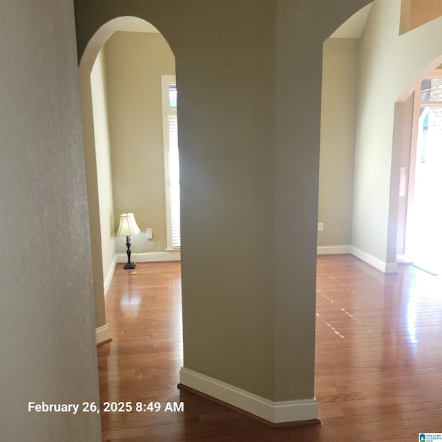 corridor with arched walkways, wood finished floors, and baseboards