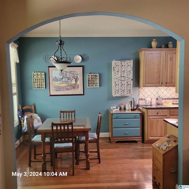 dining space with light wood finished floors, baseboards, arched walkways, and crown molding