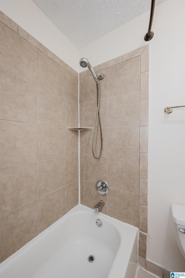 bathroom featuring a textured ceiling, toilet, and tiled shower / bath