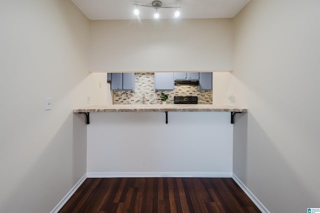 kitchen with a kitchen bar, kitchen peninsula, decorative backsplash, and dark wood-type flooring