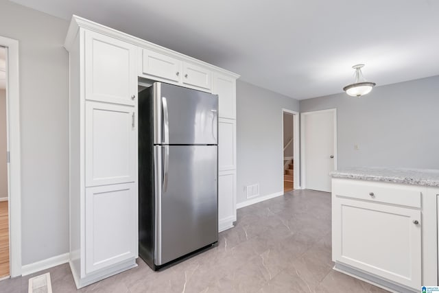 kitchen featuring white cabinets, light stone countertops, and stainless steel refrigerator