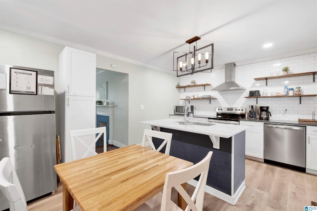 kitchen featuring white cabinetry, wall chimney exhaust hood, decorative light fixtures, and appliances with stainless steel finishes