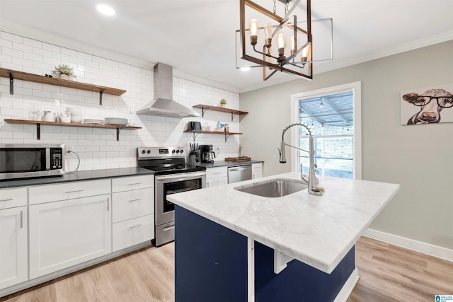 kitchen with wall chimney exhaust hood, stainless steel appliances, an island with sink, light hardwood / wood-style floors, and white cabinets