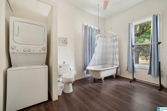 bathroom with hardwood / wood-style floors, stacked washer and clothes dryer, ceiling fan, toilet, and a tub to relax in