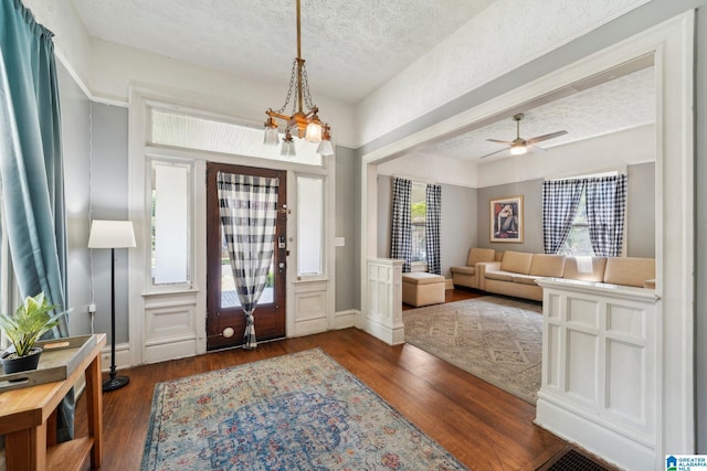 foyer featuring dark hardwood / wood-style flooring, ceiling fan with notable chandelier, and a textured ceiling