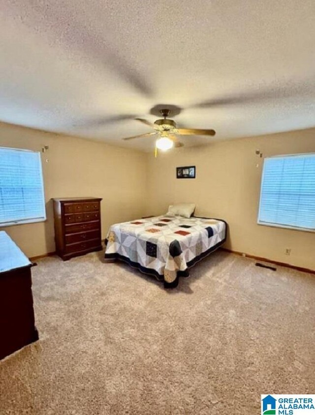 bedroom featuring ceiling fan, light colored carpet, and a textured ceiling