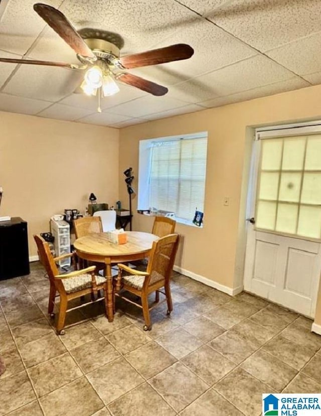 tiled dining space with ceiling fan and a drop ceiling