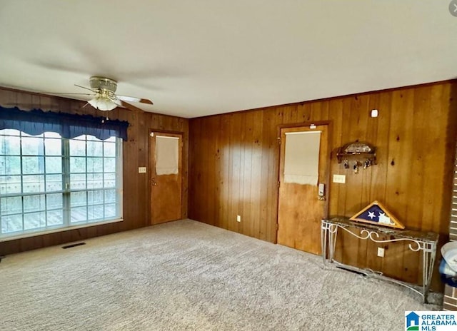 carpeted empty room with wood walls and ceiling fan