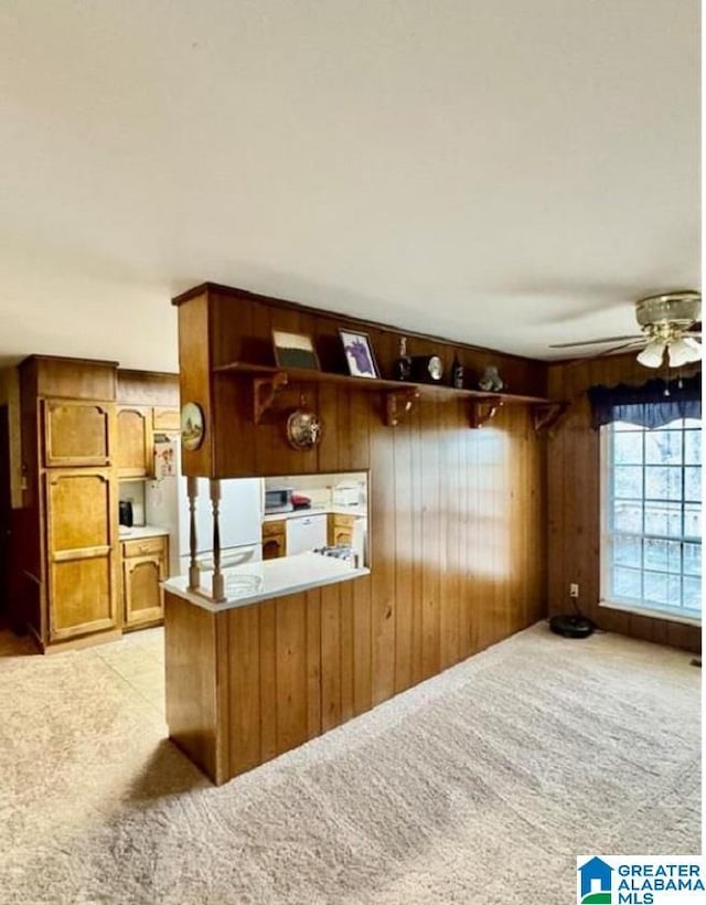 interior space with kitchen peninsula, ceiling fan, wood walls, and white refrigerator