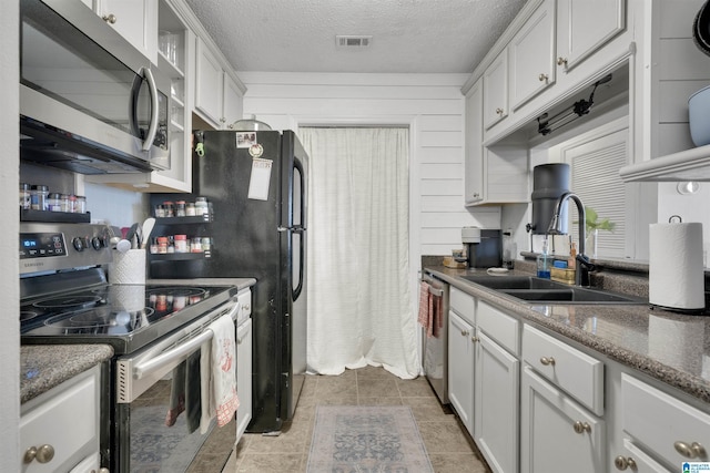 kitchen featuring sink, dark stone counters, a textured ceiling, wooden walls, and appliances with stainless steel finishes