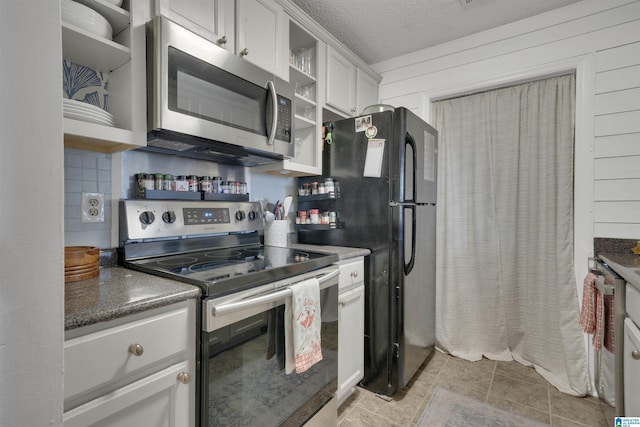 kitchen with a textured ceiling, stainless steel appliances, white cabinetry, and wooden walls