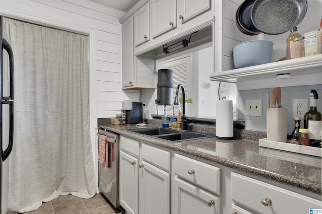 kitchen featuring stainless steel dishwasher, wood walls, white cabinets, and sink