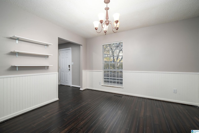 unfurnished dining area with a textured ceiling, dark hardwood / wood-style floors, and a notable chandelier