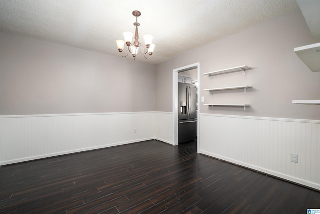 unfurnished room with a textured ceiling, dark wood-type flooring, and an inviting chandelier