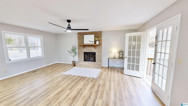 unfurnished living room with ceiling fan, french doors, light hardwood / wood-style floors, and a brick fireplace