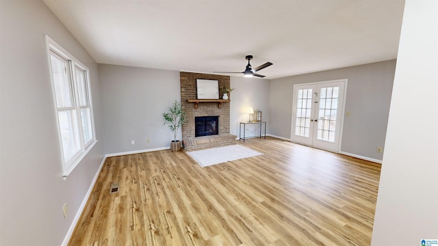 unfurnished living room featuring ceiling fan, light hardwood / wood-style flooring, french doors, and a brick fireplace