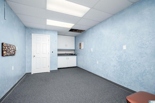 basement featuring dark carpet, a drop ceiling, and sink