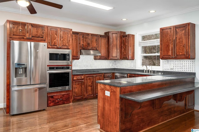 kitchen featuring stainless steel appliances, kitchen peninsula, wood-type flooring, decorative backsplash, and ornamental molding