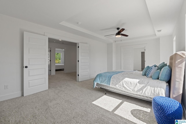 bedroom featuring light carpet, a tray ceiling, and ceiling fan