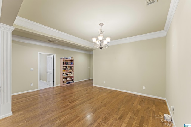 empty room with ornate columns, crown molding, a notable chandelier, and hardwood / wood-style flooring