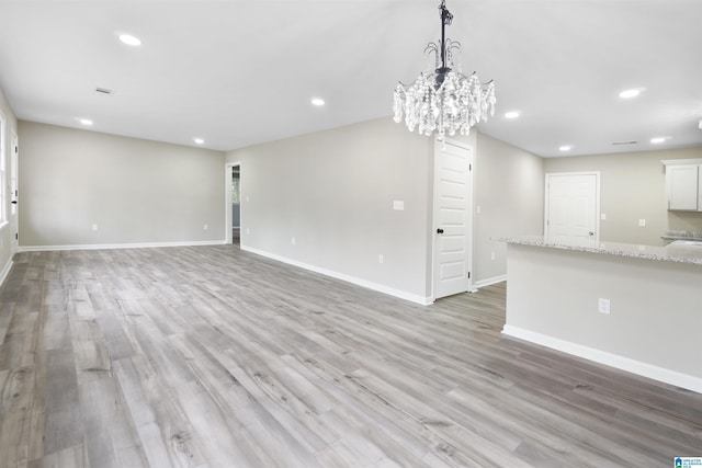 unfurnished living room featuring an inviting chandelier and light hardwood / wood-style flooring