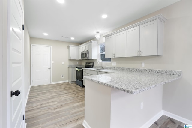 kitchen featuring black electric range oven, sink, light stone countertops, light hardwood / wood-style floors, and white cabinetry