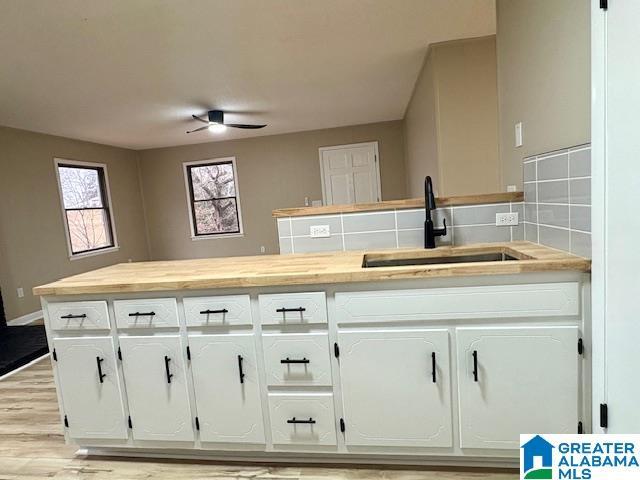 kitchen featuring decorative backsplash, white cabinetry, sink, and light hardwood / wood-style flooring