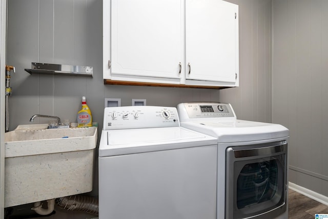 washroom with cabinets, sink, wooden walls, independent washer and dryer, and dark hardwood / wood-style flooring