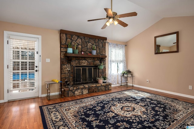 living room featuring hardwood / wood-style floors, vaulted ceiling, a healthy amount of sunlight, and a stone fireplace